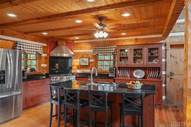 kitchen with wall chimney range hood, stainless steel fridge, wooden walls, and plenty of natural light