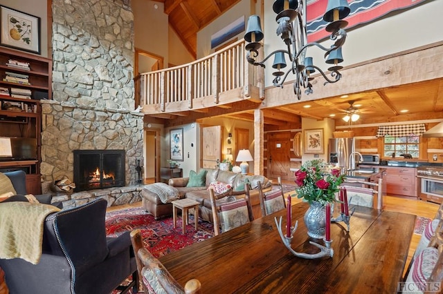 dining room featuring a stone fireplace, hardwood / wood-style floors, high vaulted ceiling, wooden ceiling, and beam ceiling