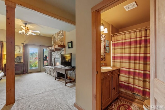 bathroom with beamed ceiling, vanity, a stone fireplace, and ceiling fan