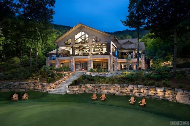 back house at dusk featuring a balcony and a lawn