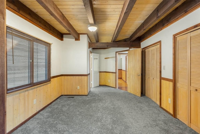 unfurnished bedroom featuring wood walls, dark colored carpet, wood ceiling, multiple closets, and beam ceiling