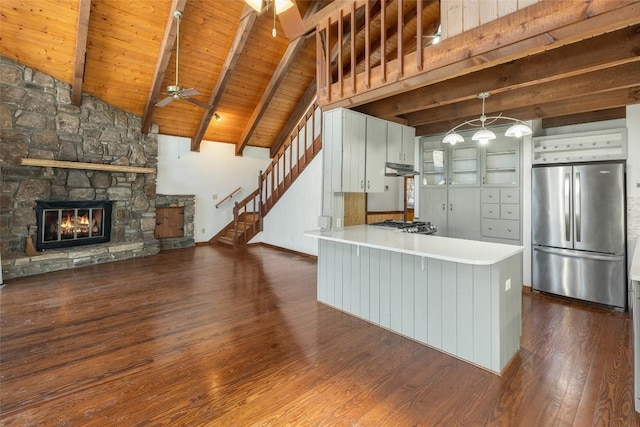 kitchen with stainless steel refrigerator, beam ceiling, a fireplace, dark hardwood / wood-style flooring, and kitchen peninsula