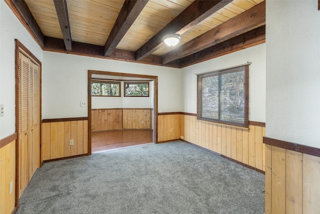 carpeted empty room featuring beamed ceiling, plenty of natural light, and wood walls