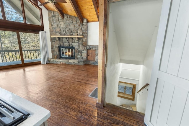 unfurnished living room featuring wood ceiling, dark wood-type flooring, ceiling fan, vaulted ceiling with beams, and a stone fireplace