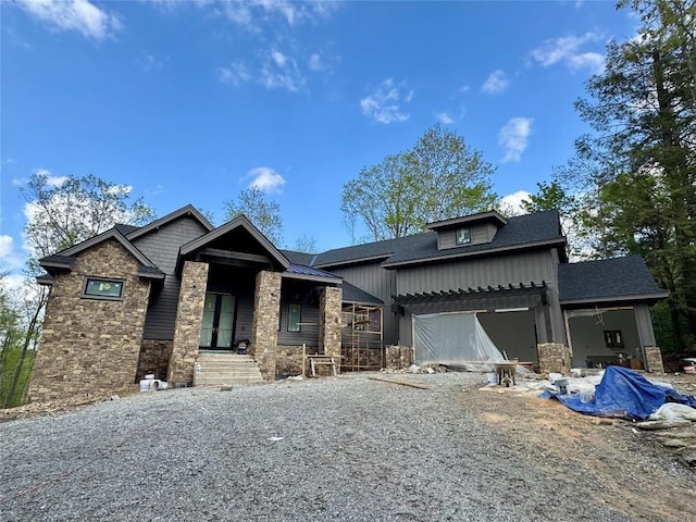 view of front of house featuring stone siding, driveway, an attached garage, board and batten siding, and roof with shingles