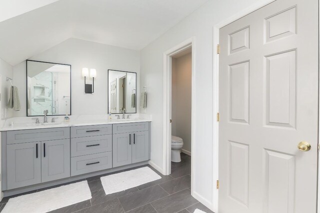 bathroom with double vanity, toilet, lofted ceiling, baseboards, and a shower