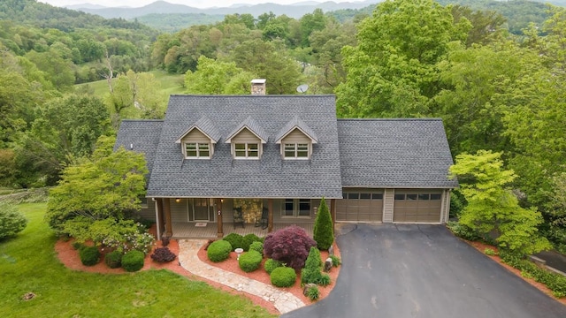 cape cod house featuring covered porch, a view of trees, a chimney, asphalt driveway, and a mountain view