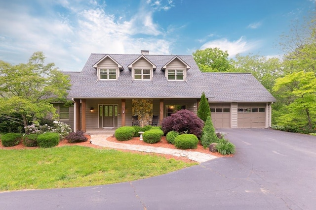 new england style home with a porch, a chimney, a garage, driveway, and a front yard