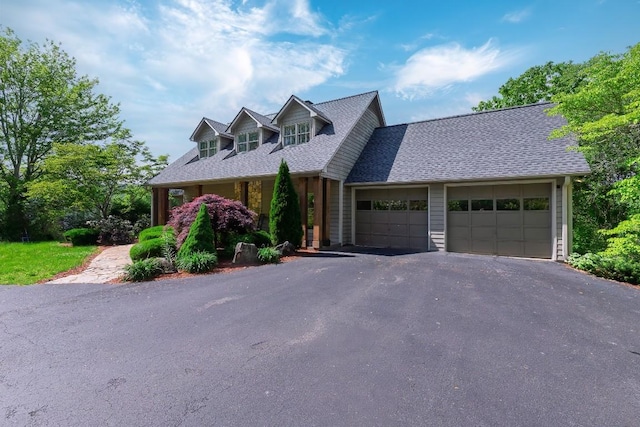 cape cod house featuring an attached garage, driveway, and roof with shingles
