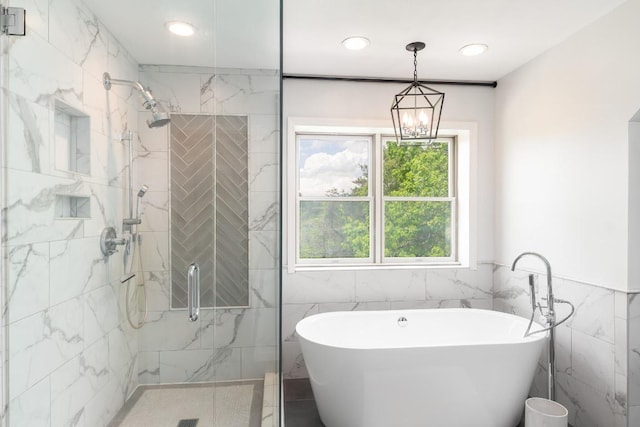 bathroom with tile walls, a stall shower, a soaking tub, a chandelier, and recessed lighting