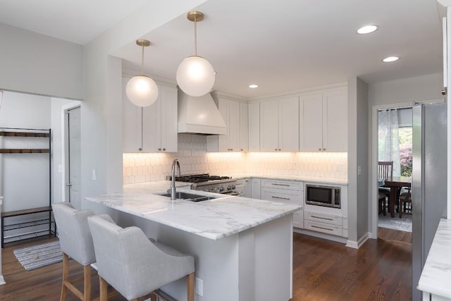 kitchen featuring stainless steel microwave, custom range hood, a peninsula, white cabinetry, and tasteful backsplash