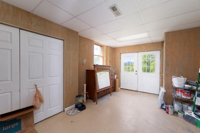 entrance foyer with a drop ceiling, concrete flooring, french doors, and wooden walls