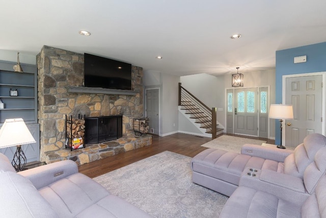living room featuring stairway, wood finished floors, a stone fireplace, baseboards, and a chandelier