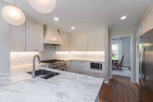 kitchen featuring custom range hood, stainless steel appliances, a sink, light stone countertops, and tasteful backsplash
