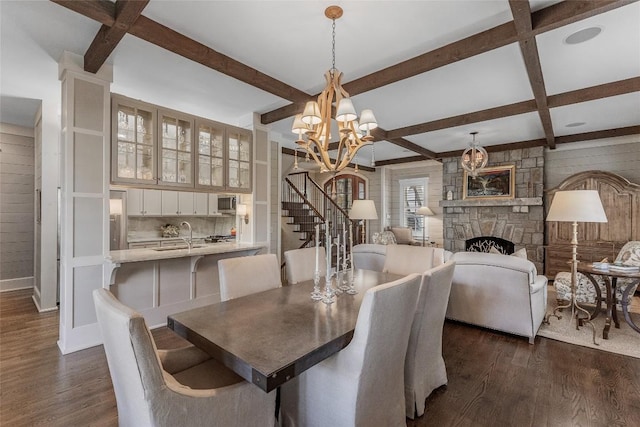 dining room featuring a stone fireplace, wood walls, beamed ceiling, a chandelier, and dark wood-type flooring