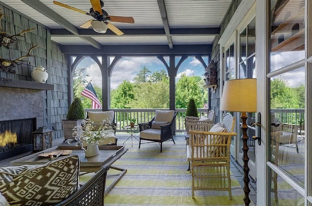 sunroom / solarium with beamed ceiling, a large fireplace, and ceiling fan