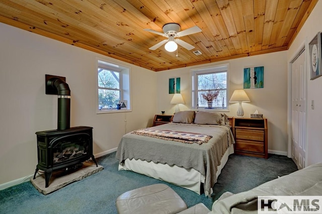 carpeted bedroom featuring a wood stove, multiple windows, wood ceiling, and baseboards