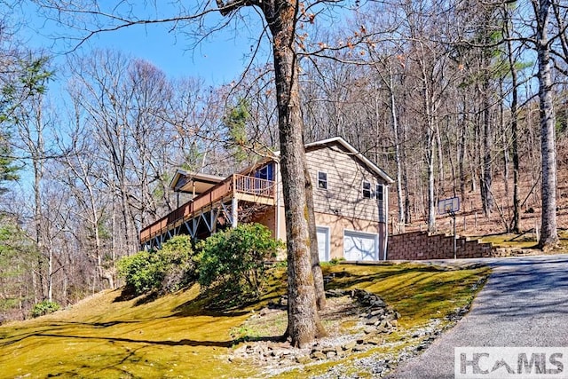 view of side of home featuring stairway, driveway, a garage, a yard, and a deck