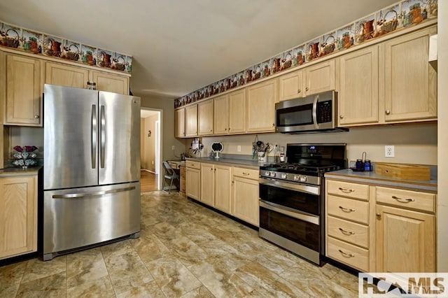 kitchen with stainless steel appliances, stone finish floor, light brown cabinetry, and dark countertops