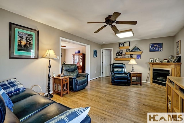 living area with light wood-style flooring, ceiling fan, a fireplace, and baseboards