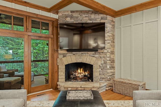 living room featuring beamed ceiling, light hardwood / wood-style floors, and a stone fireplace