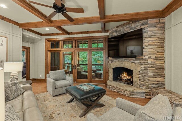 living room with ceiling fan, a stone fireplace, light hardwood / wood-style flooring, and beamed ceiling