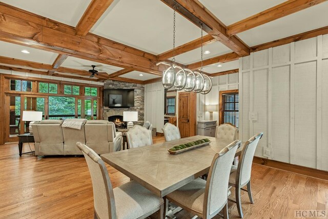 dining room with beamed ceiling, coffered ceiling, a stone fireplace, and light hardwood / wood-style flooring