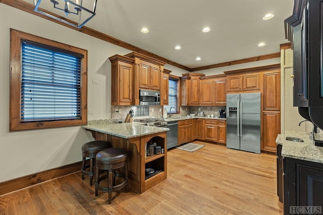 kitchen with sink, a kitchen breakfast bar, stainless steel appliances, kitchen peninsula, and light stone countertops