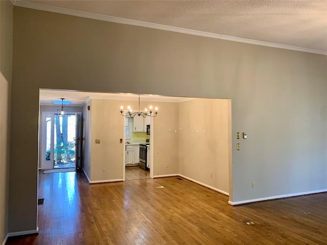 empty room with a notable chandelier, dark wood-type flooring, baseboards, and ornamental molding