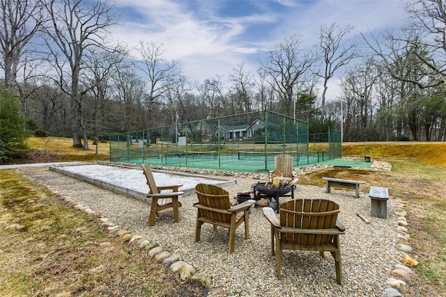 view of swimming pool with a tennis court, fence, and an outdoor fire pit