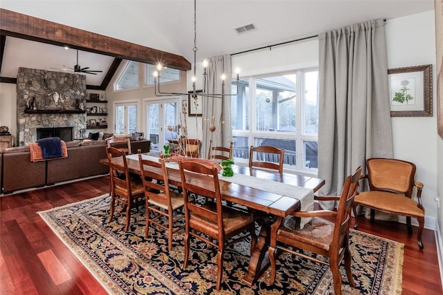 dining area featuring vaulted ceiling with beams, a stone fireplace, dark wood-type flooring, and visible vents