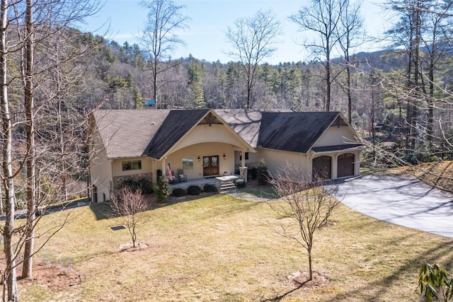 view of front of house with covered porch, a front yard, a garage, driveway, and a forest view