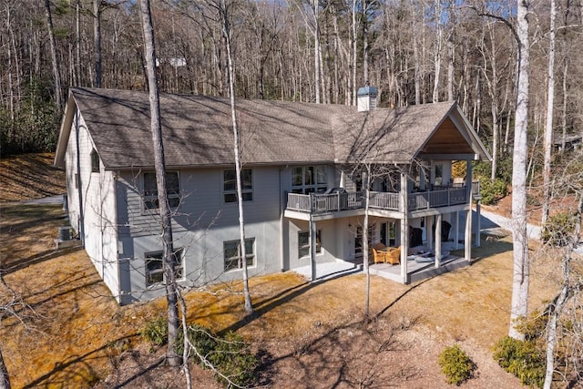 rear view of house with a patio, a chimney, a wooden deck, and a view of trees