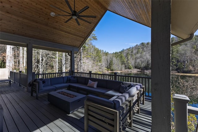 deck featuring ceiling fan, a wooded view, and an outdoor living space with a fire pit