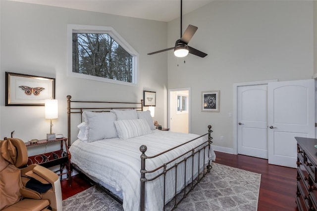 bedroom featuring a towering ceiling, ceiling fan, baseboards, and wood finished floors