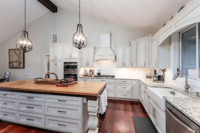 kitchen featuring custom range hood, wood counters, appliances with stainless steel finishes, dark wood-style flooring, and a sink