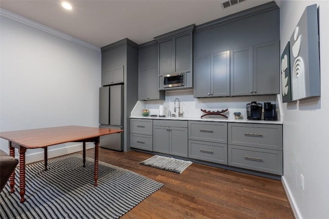 kitchen with gray cabinetry, stainless steel appliances, dark wood-type flooring, a sink, and light countertops