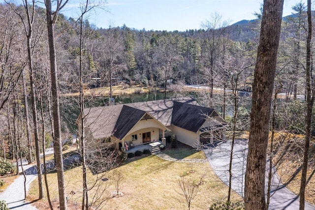 view of front of home with driveway, a forest view, a front lawn, and covered porch