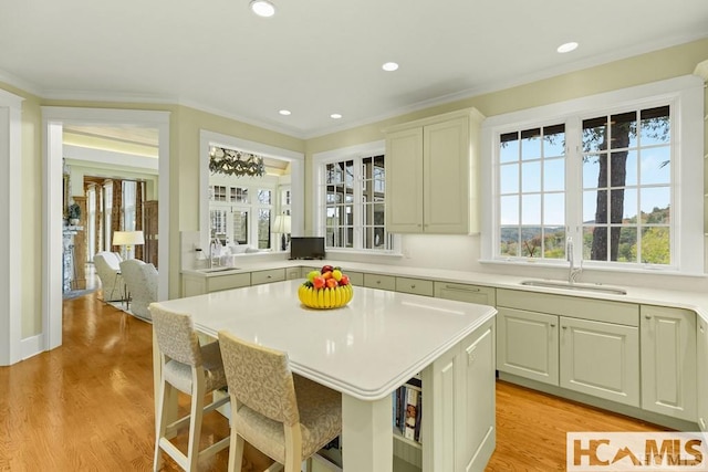 kitchen with a sink, light countertops, light wood-type flooring, a breakfast bar, and ornamental molding