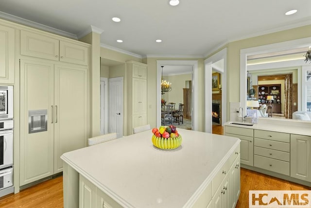 kitchen featuring a sink, light countertops, a lit fireplace, ornamental molding, and light wood finished floors