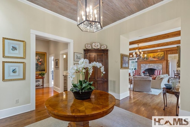 entrance foyer featuring a chandelier, wood finished floors, baseboards, crown molding, and a stone fireplace