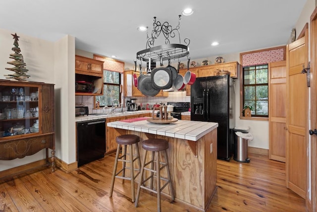 kitchen with tile countertops, black appliances, plenty of natural light, and a kitchen island