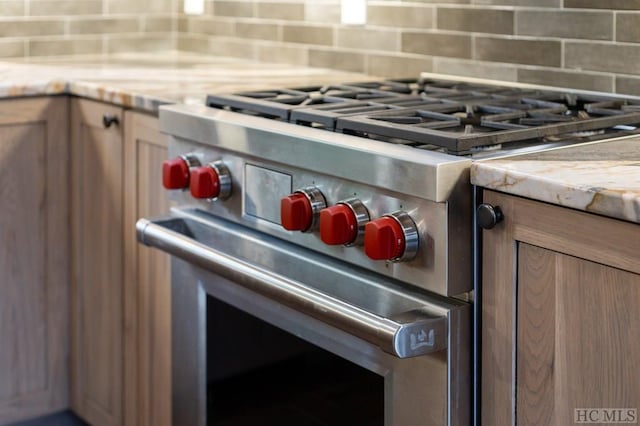 interior details with tasteful backsplash, light brown cabinetry, and high end stove