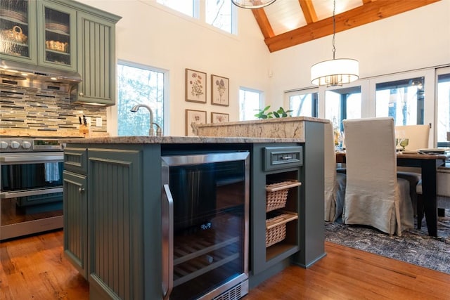 kitchen with green cabinets, wine cooler, under cabinet range hood, double oven range, and wood finished floors