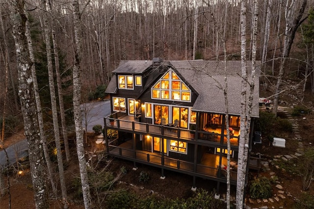 back of house featuring a forest view and roof with shingles