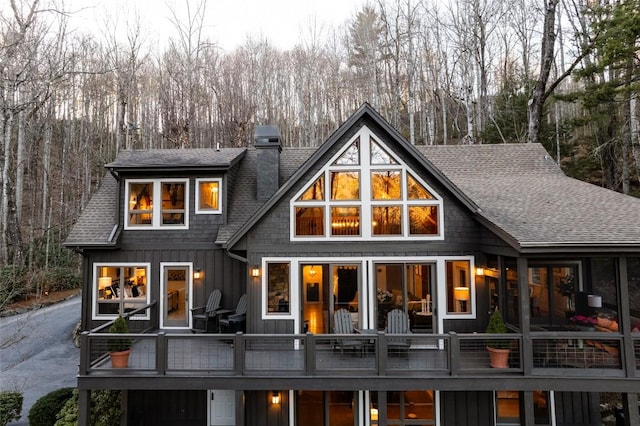 rear view of property featuring board and batten siding, a chimney, and roof with shingles