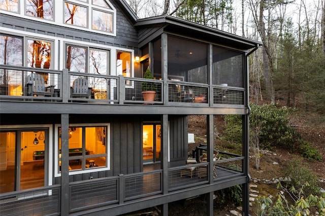 back of property with board and batten siding, a balcony, and a sunroom