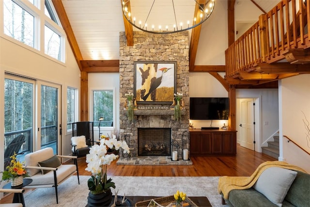 living room with a chandelier, a stone fireplace, a healthy amount of sunlight, and wood finished floors