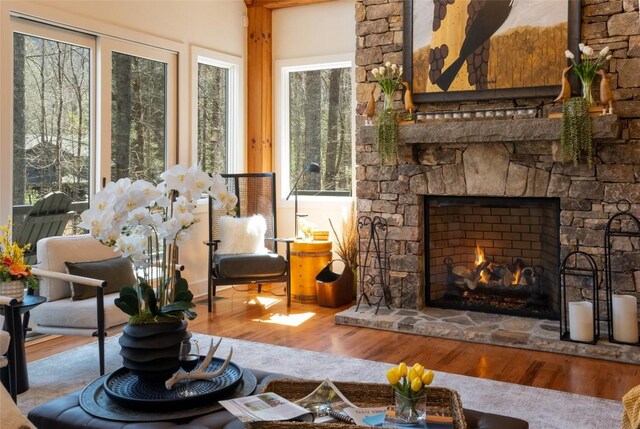 living area with a stone fireplace, vaulted ceiling with beams, and wood finished floors