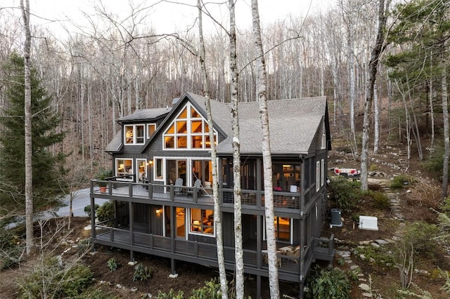 rear view of property with a view of trees, central AC, roof with shingles, a sunroom, and a chimney